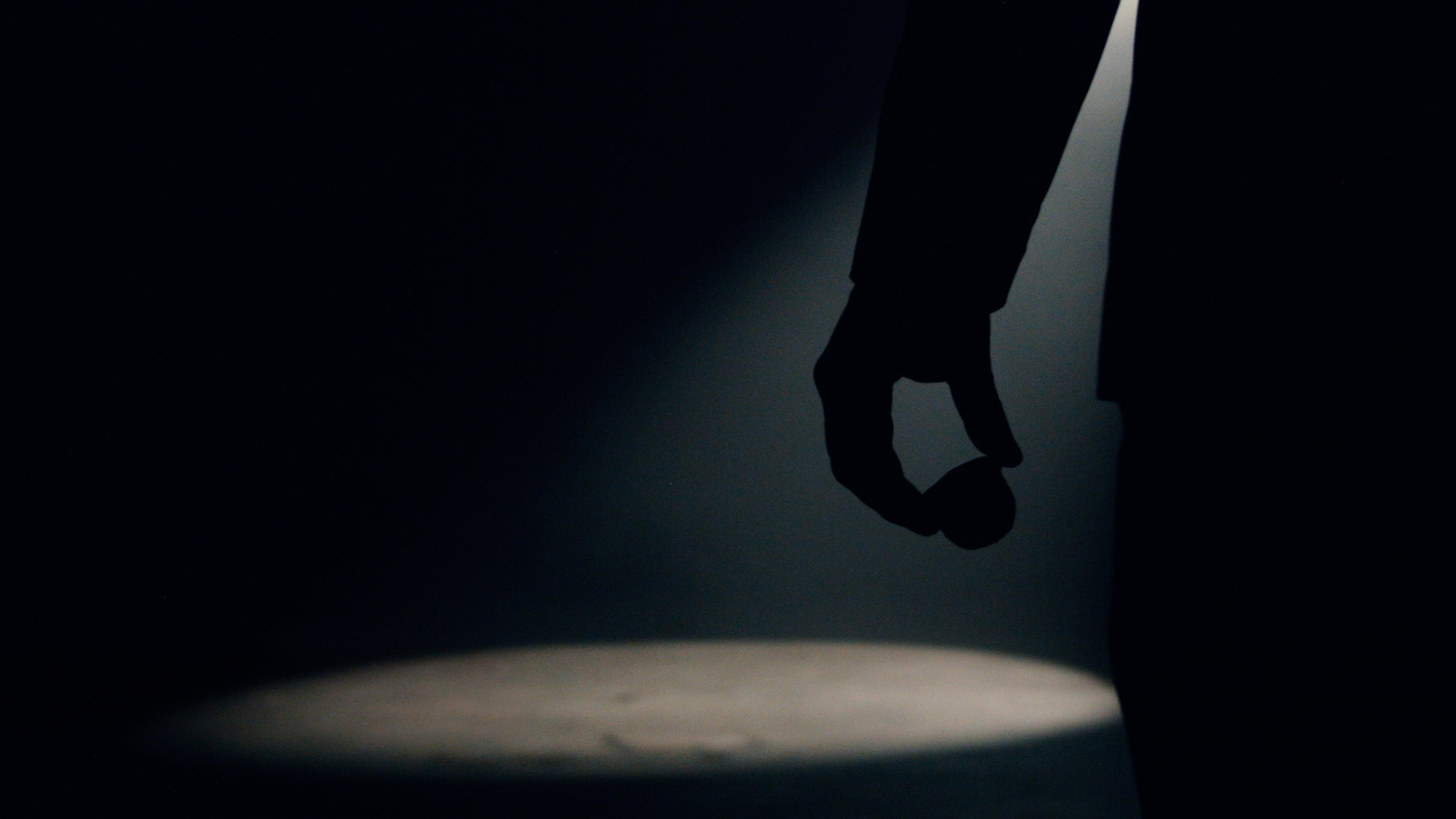 silhouette of a man's hand holding a coffee pod against a dark background - only broken up by the cone of a spotlight cutting through the atmosphere